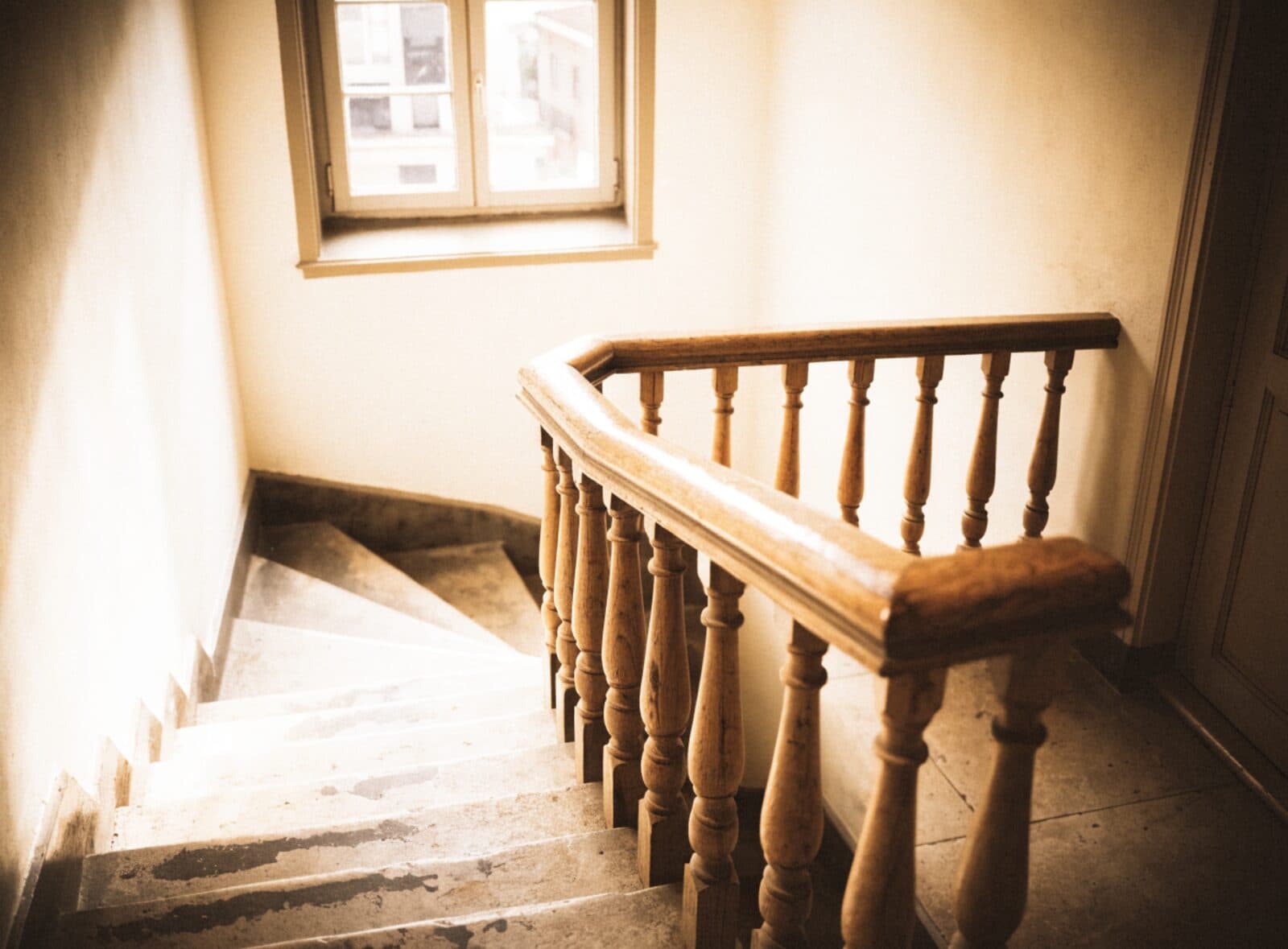 Treppenhaus eines Altbaus mit hölzernem Geländer im Tageslicht, Symbolbild