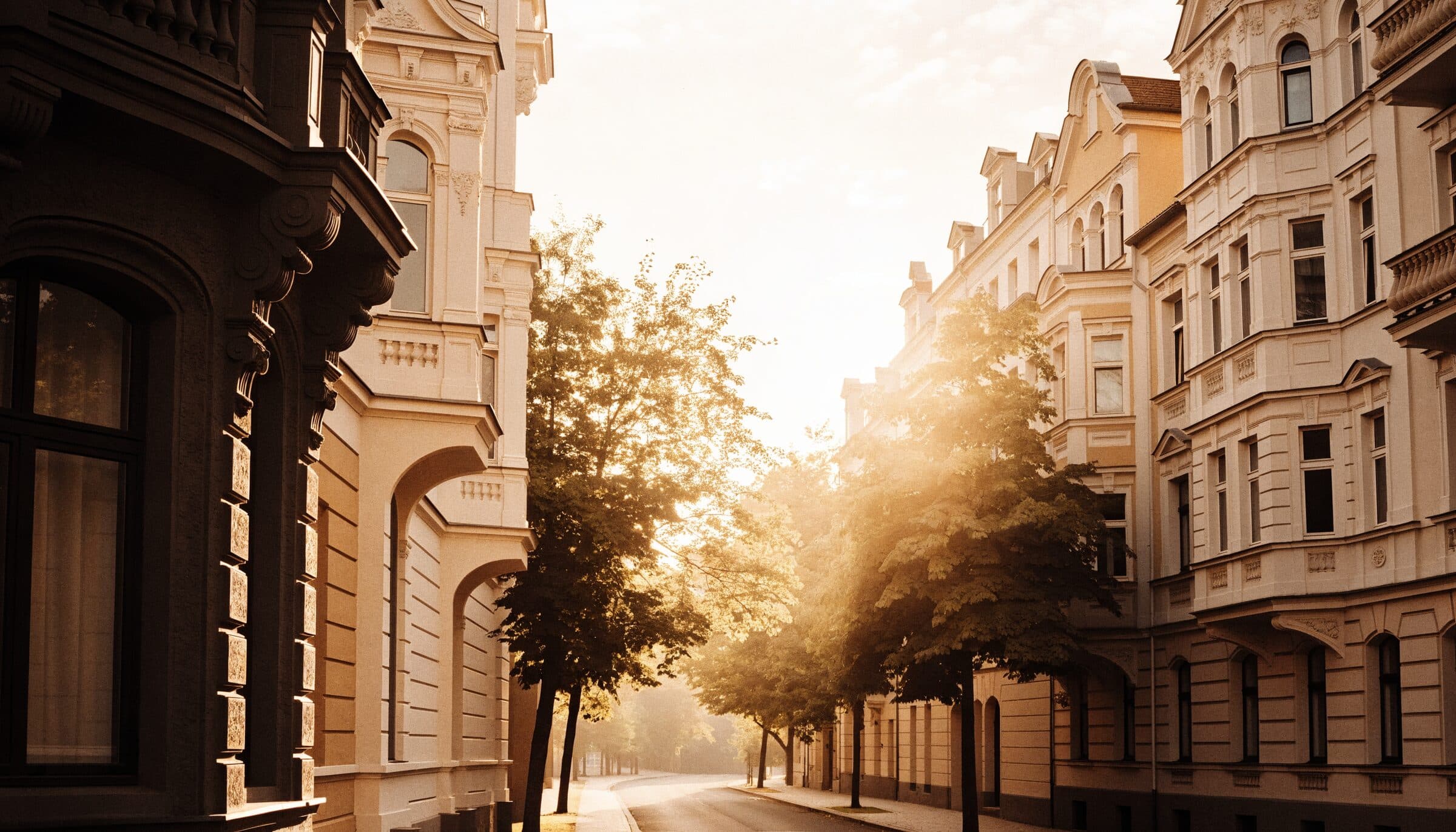 Baumgesäumte Straße mit Gründerzeithäusern im Abendlicht, Symbolbild
